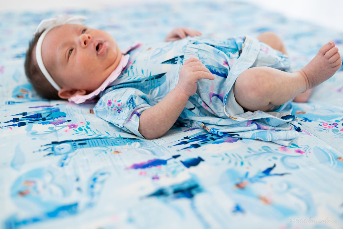 Baby Princess Dress – The Wish Collection – on-model, newborn lying on back in blue castle-print dress