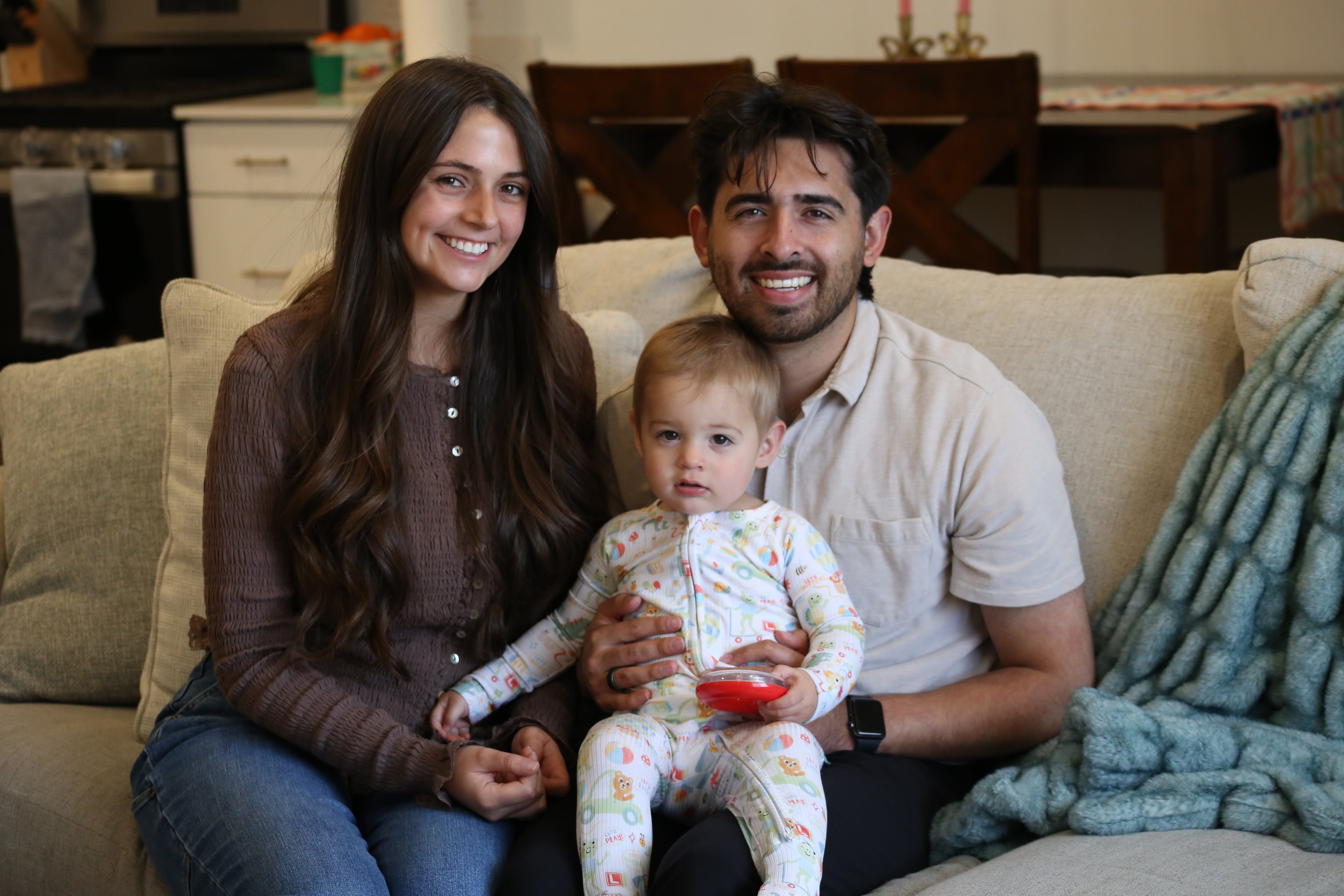 Family of three sitting on a couch in a home setting