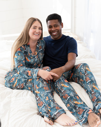 Couple sitting on a bed, woman in Woodland Wonder pajama set and man in matching pajama pants