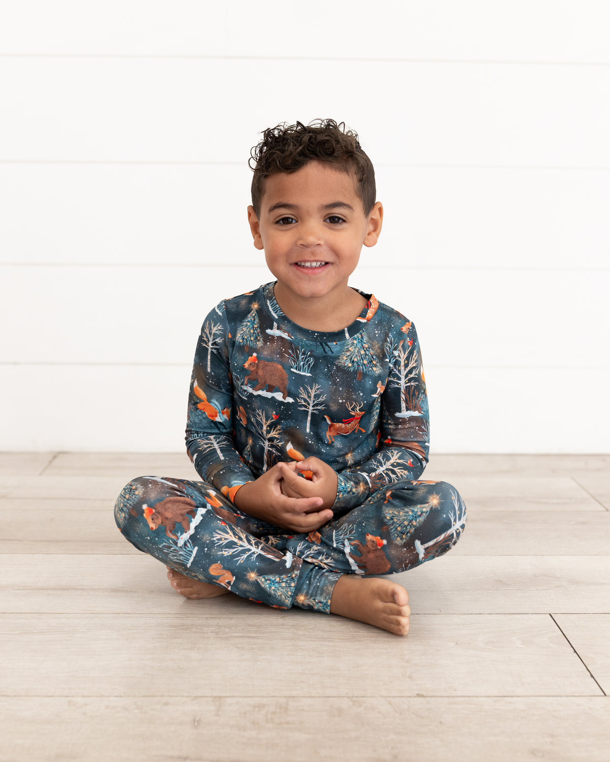 Young boy sitting cross-legged wearing Woodland Wonder bamboo kids pajamas