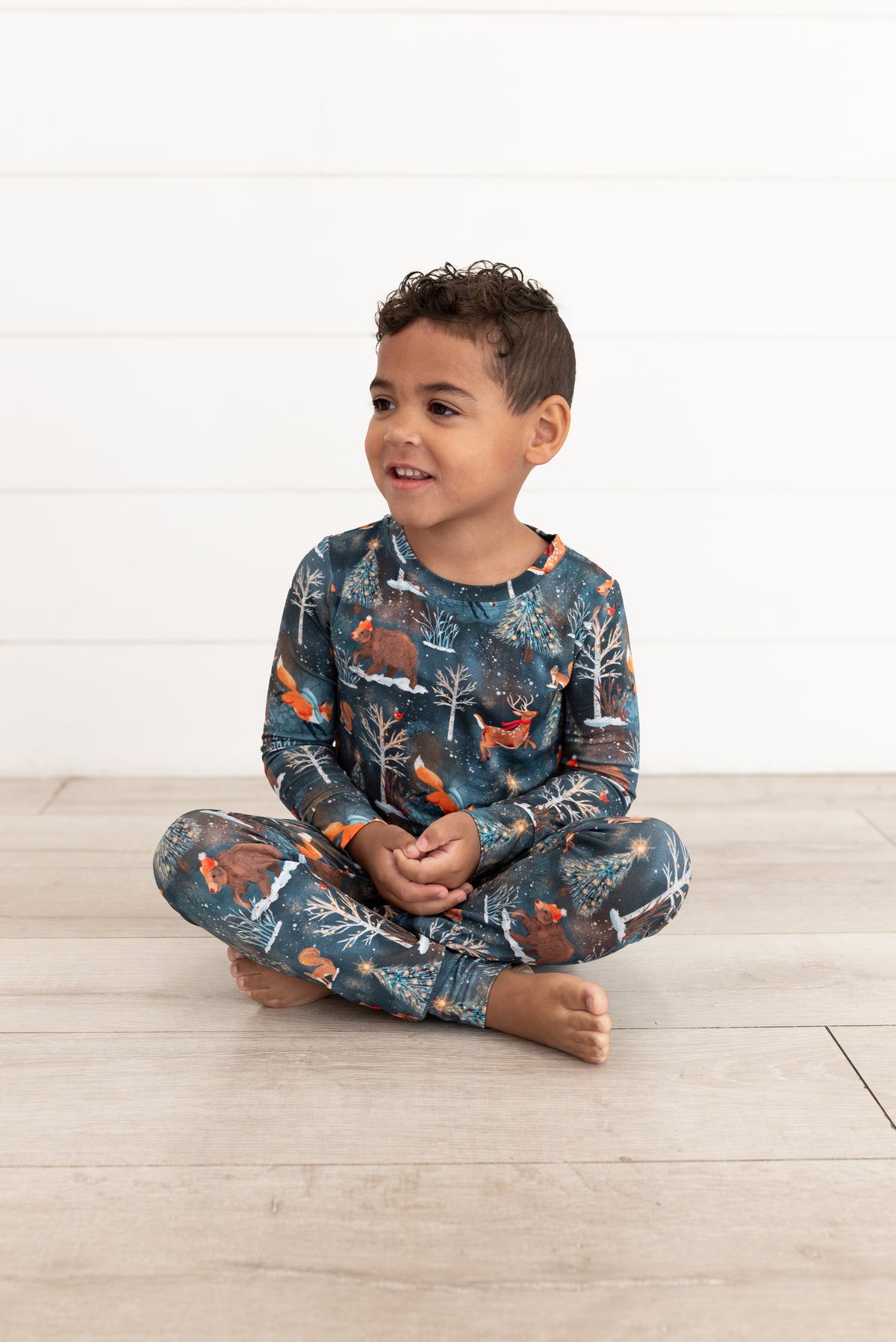 Young boy sitting cross-legged on the floor wearing Woodland Wonder bamboo kids pajamas