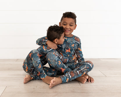 Two young boys sitting together, one hugging the other, in matching Woodland Wonder bamboo pajamas