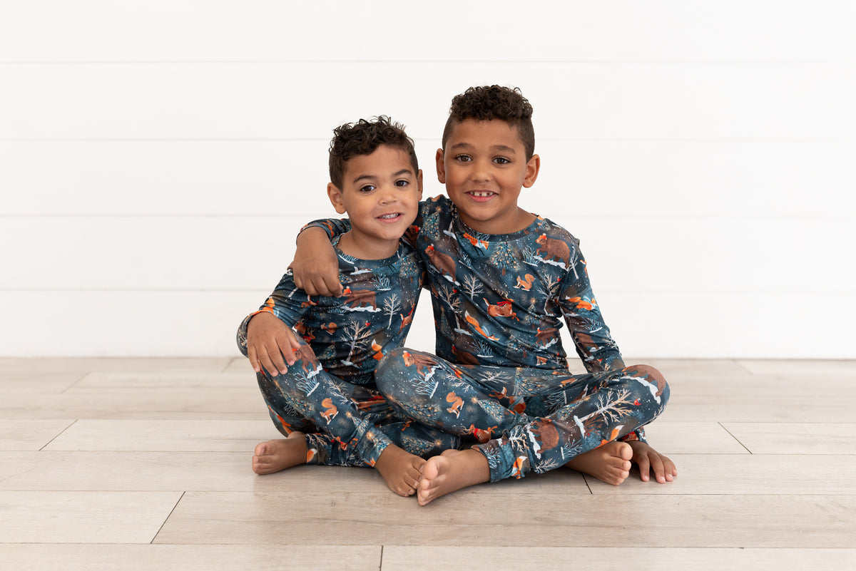 Two young boys sitting cross-legged together in matching Woodland Wonder bamboo pajamas