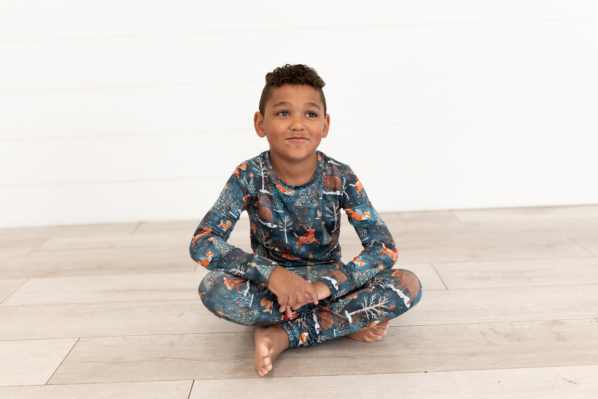 Young boy sitting cross-legged and smiling in Woodland Wonder bamboo kids pajamas