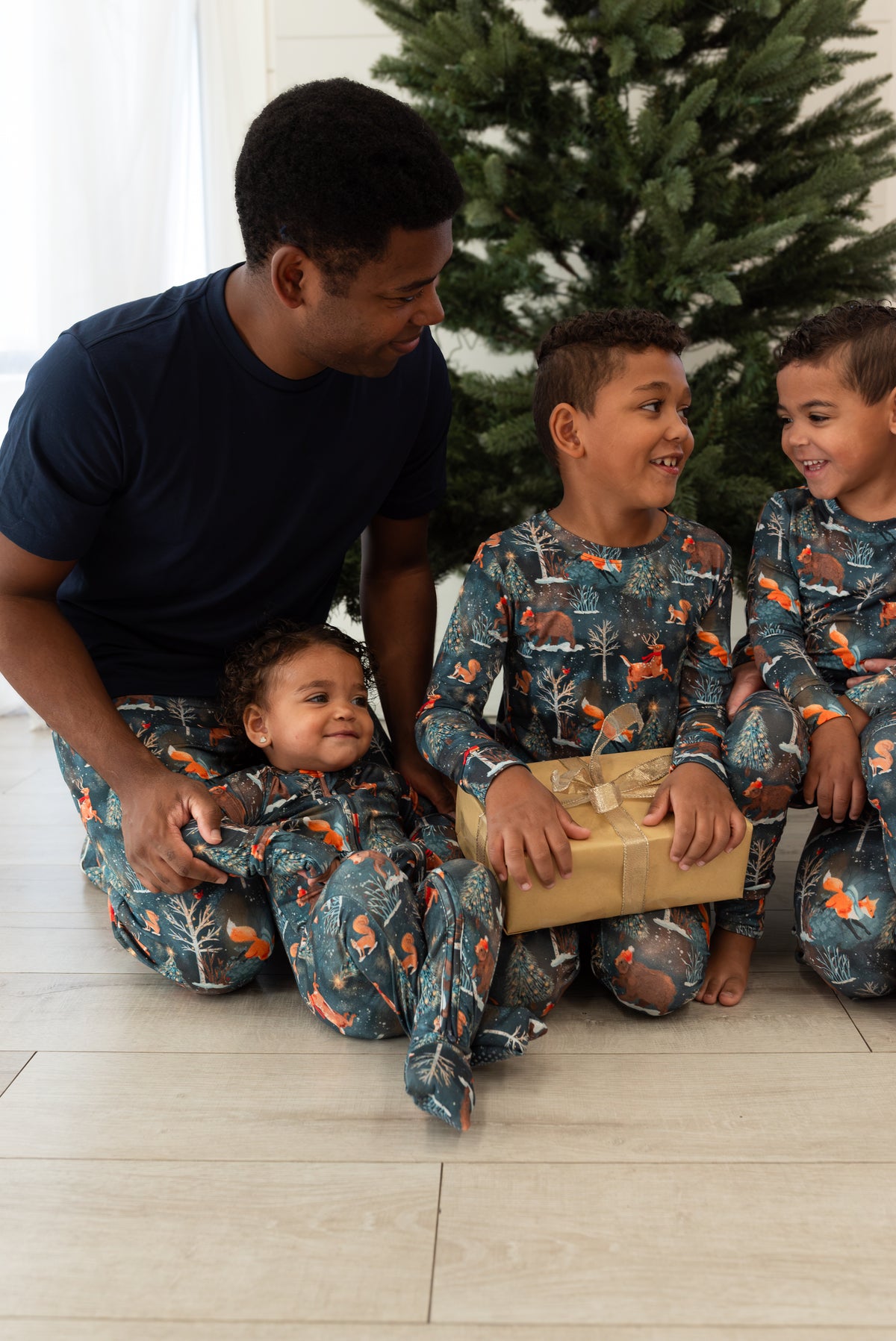 Dad with three kids in matching Woodland Wonder bamboo Christmas pajamas by a Christmas tree