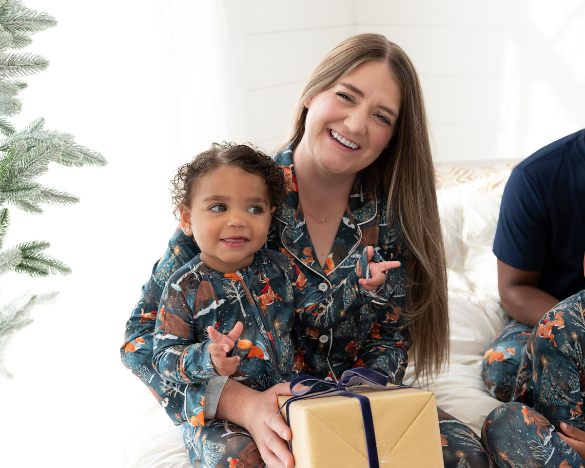 Mom holding a toddler in matching Woodland Wonder bamboo pajamas with a wrapped gift