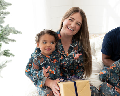 Mom holding a toddler in matching Woodland Wonder bamboo pajamas with a wrapped gift