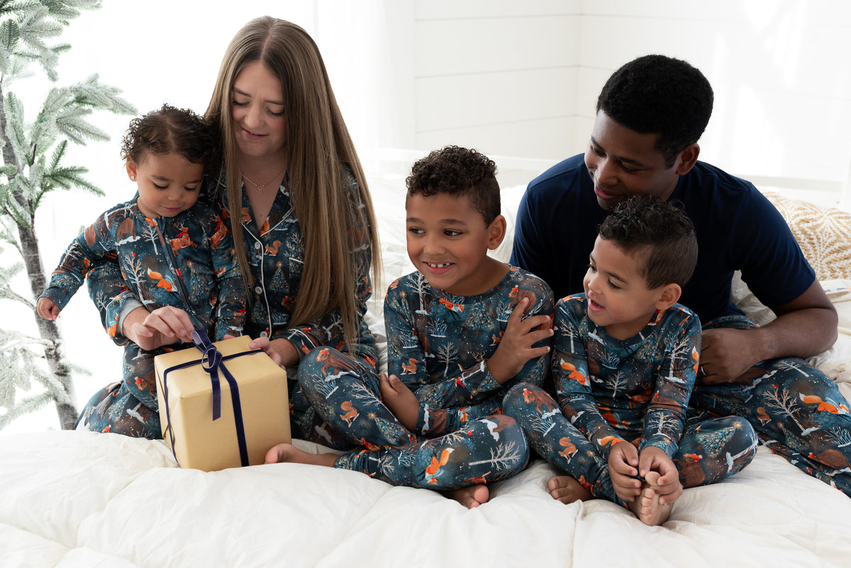 Whole family wearing matching Woodland Wonder bamboo Christmas pajamas on a bed