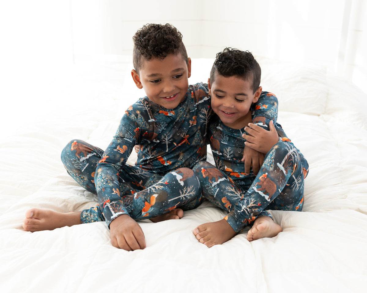 Two young boys sitting together on a bed in matching Woodland Wonder bamboo pajamas