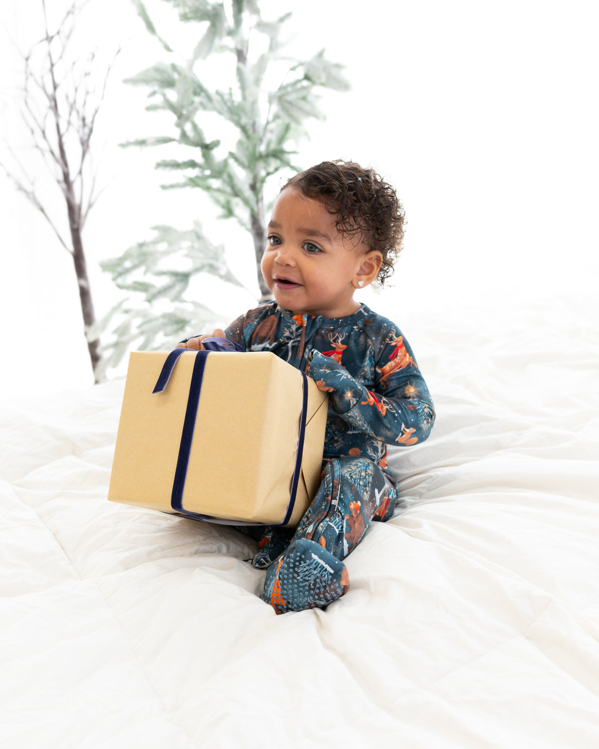 Toddler sitting on a bed holding a gift box wearing Woodland Wonder bamboo baby zip pajamas