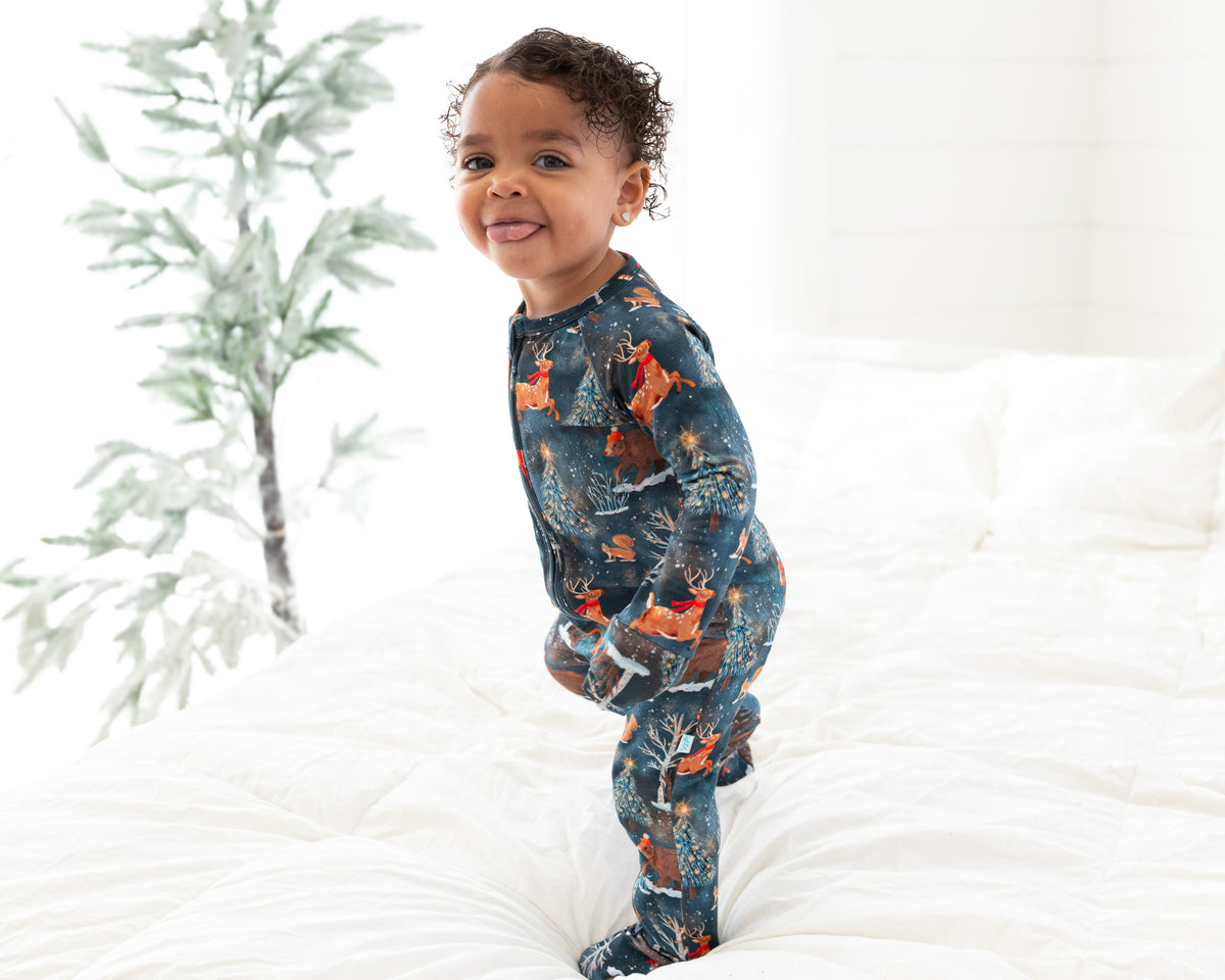 Toddler standing on a bed in profile wearing Woodland Wonder bamboo baby zip pajamas