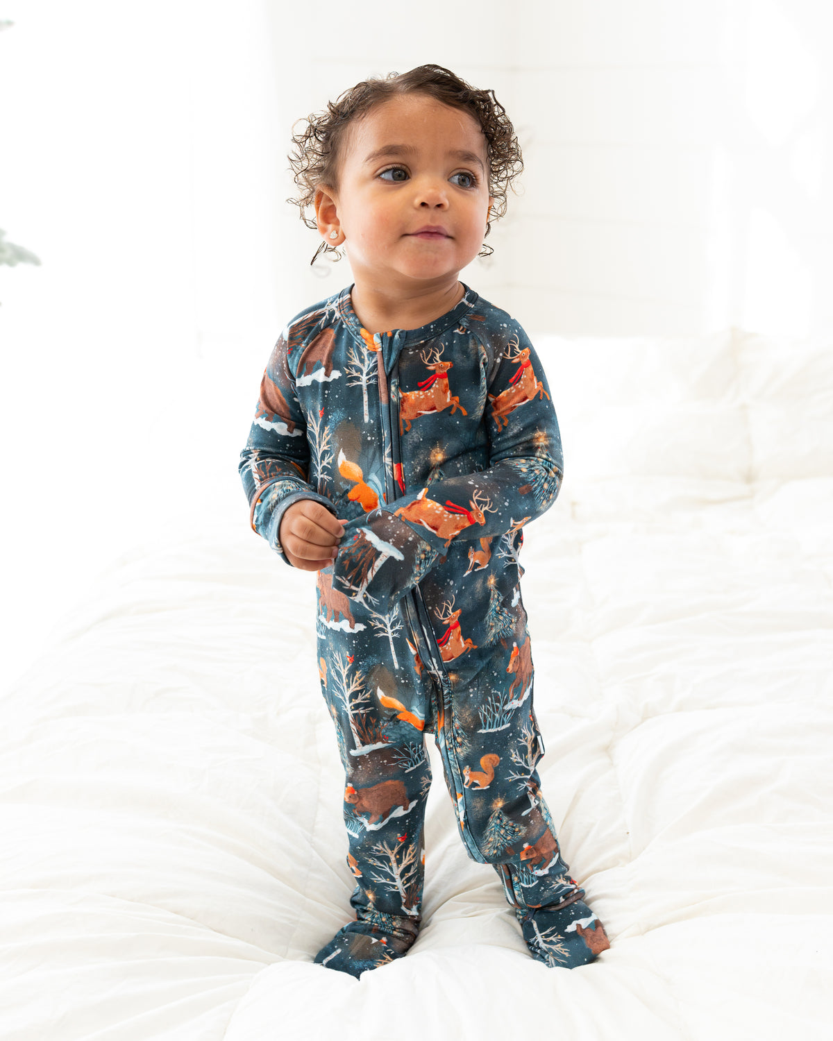 Toddler standing on a bed facing the camera in Woodland Wonder bamboo baby zip pajamas