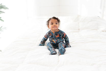 Toddler sitting on a white bed wearing Woodland Wonder bamboo baby zip pajamas