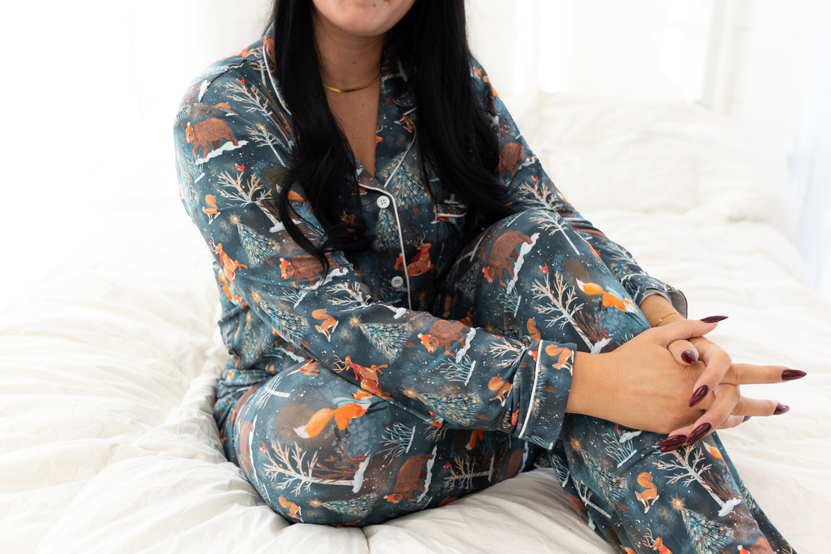 Woman sitting on a bed wearing the Woodland Wonder bamboo women's pajama set