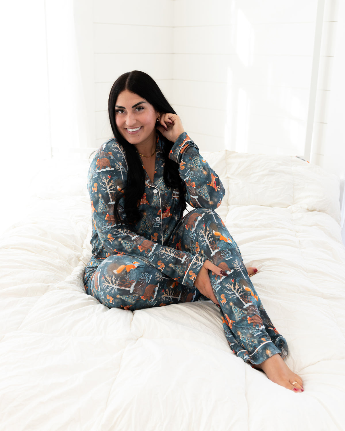 Woman sitting on a bed wearing the Woodland Wonder bamboo women's pajama shirt
