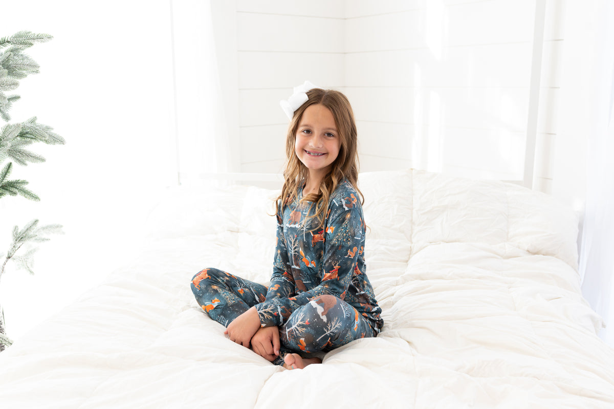 Teen girl sitting on a bed wearing Woodland Wonder bamboo teen two-piece pajamas