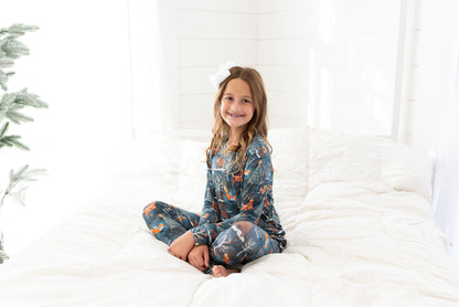 Teen girl sitting on a bed wearing Woodland Wonder bamboo teen two-piece pajamas