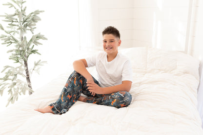 Teen boy sitting on a bed wearing Woodland Wonder bamboo pajama pants