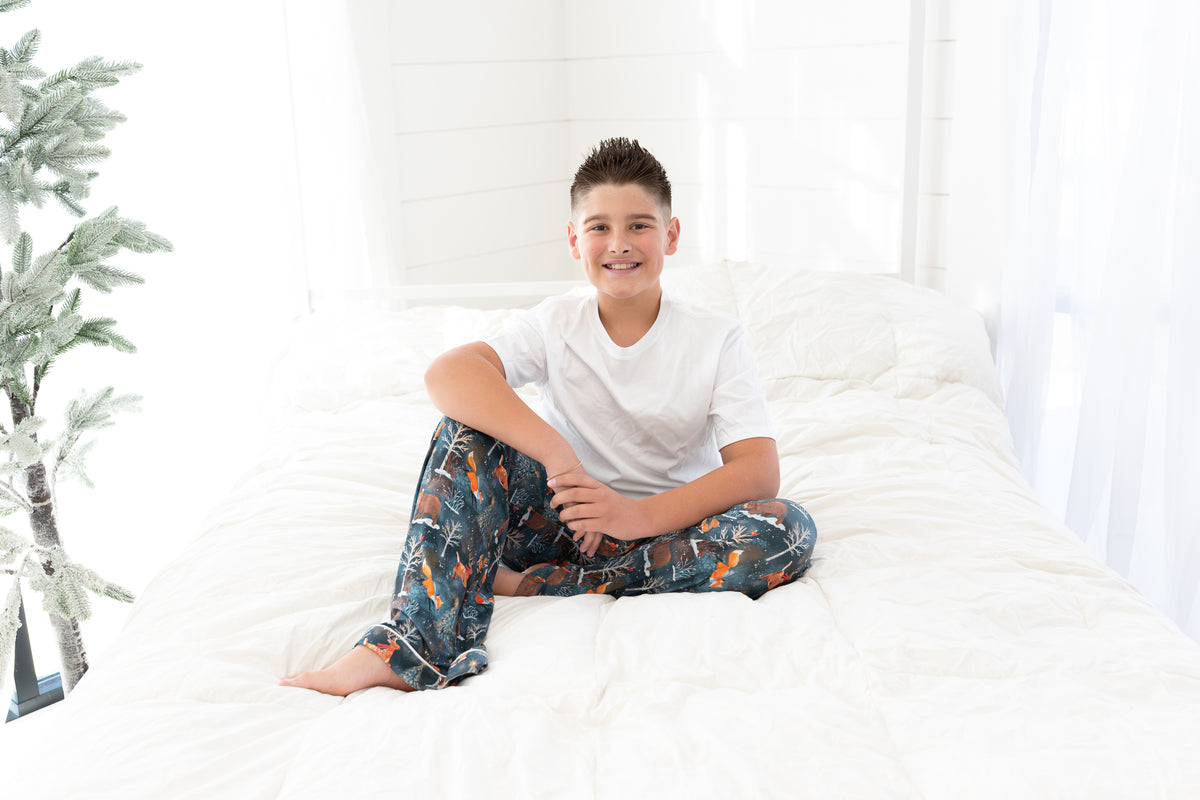 Boy sitting on a bed wearing a white t-shirt with Woodland Wonder bamboo pajama pants