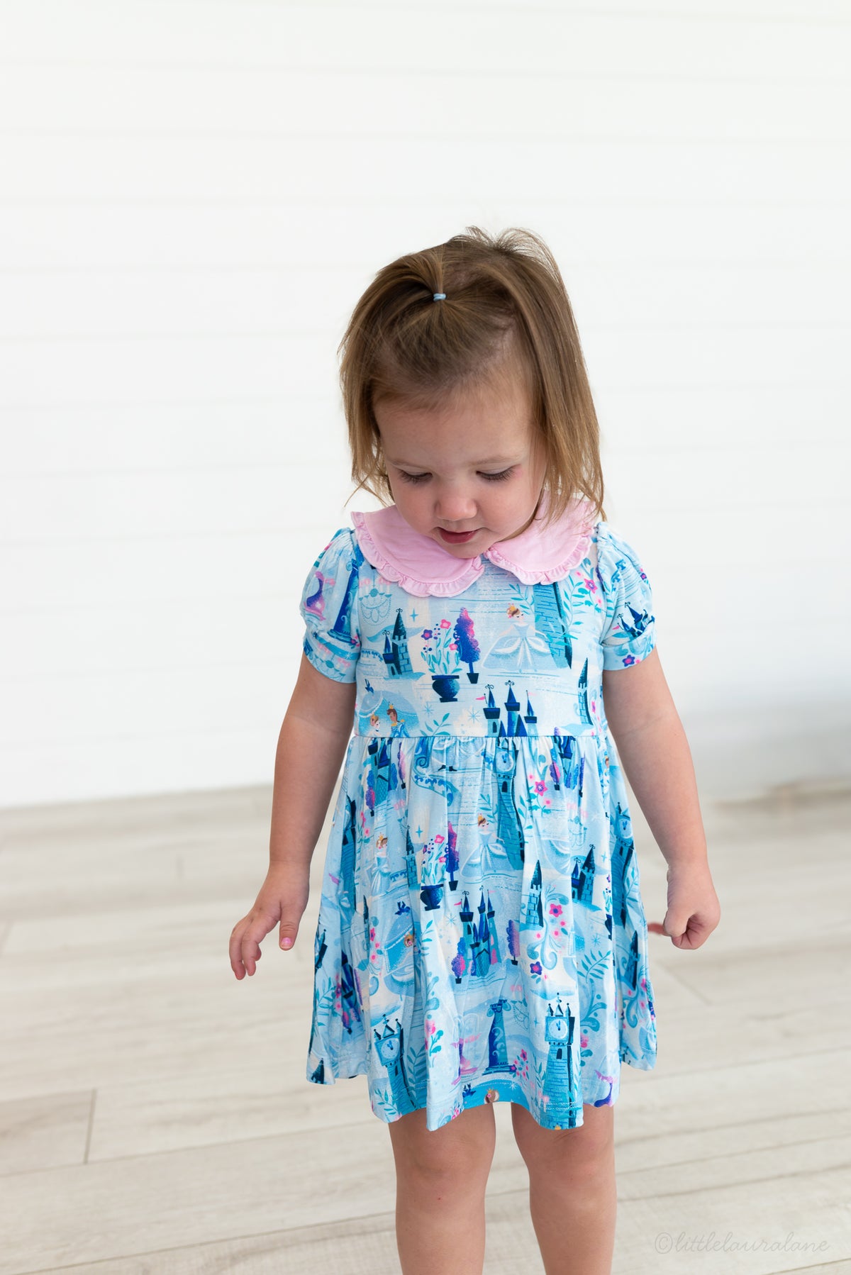 Baby Princess Dress – The Wish Collection – on-model, toddler in blue castle-print dress, pink collar, looking down
