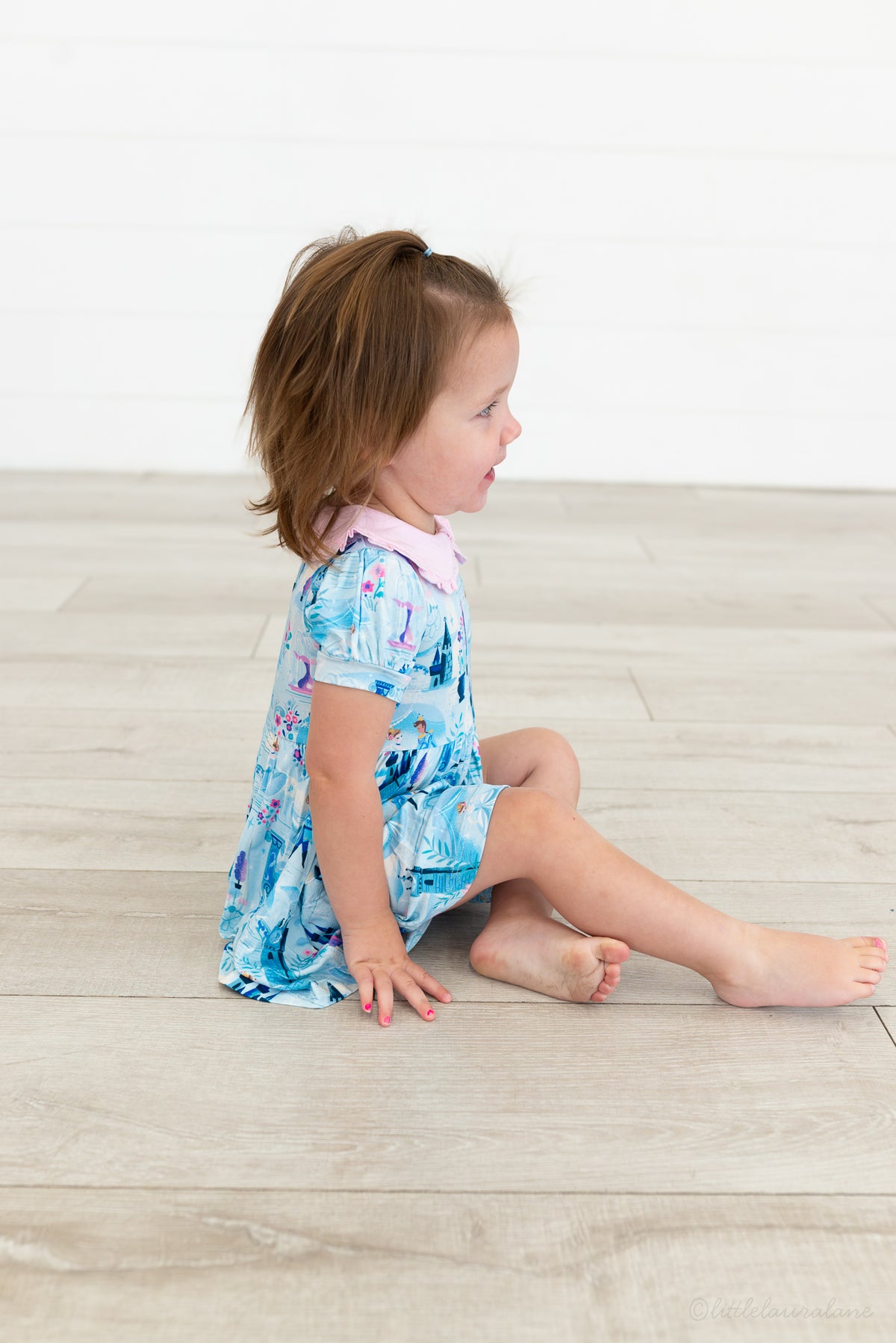 Baby Princess Dress – The Wish Collection – on-model, toddler sitting on floor in blue castle-print dress with pink collar