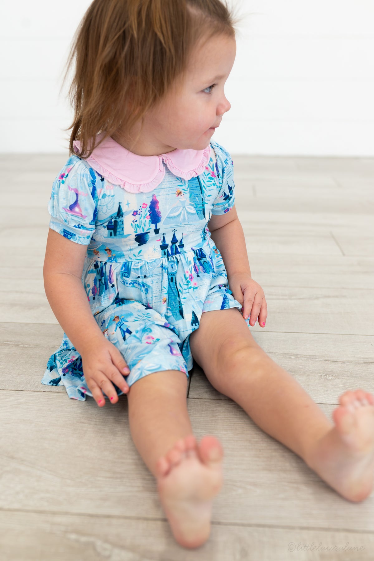 Baby Princess Dress – The Wish Collection – on-model, toddler sitting in blue castle-print dress with pink Peter Pan collar