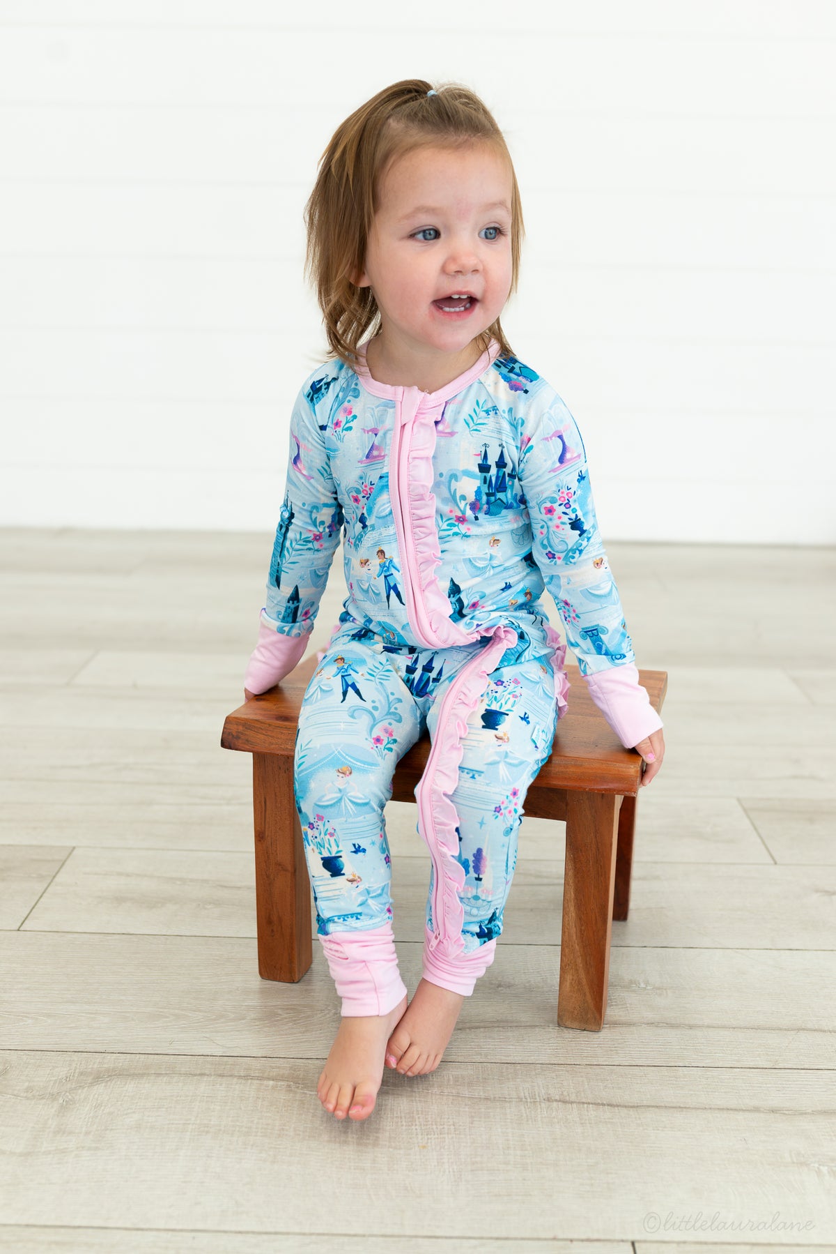 Baby Princess Pajama – The Wish Collection – on-model, toddler sitting on stool in blue castle-print zip pajama