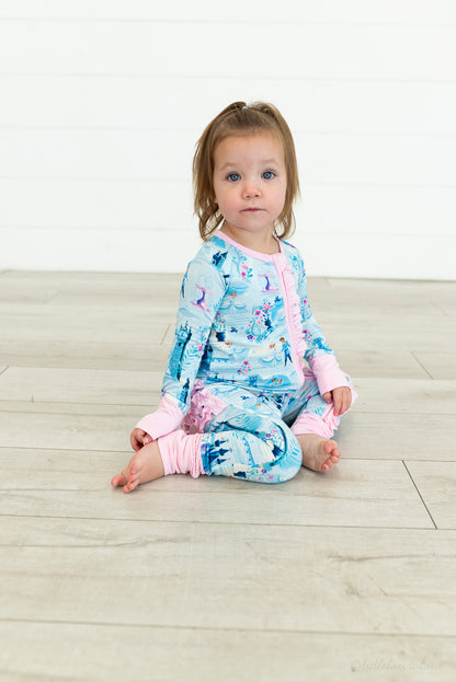 Baby Princess Pajama – The Wish Collection – on-model, toddler sitting cross-legged in blue castle-print zip pajama