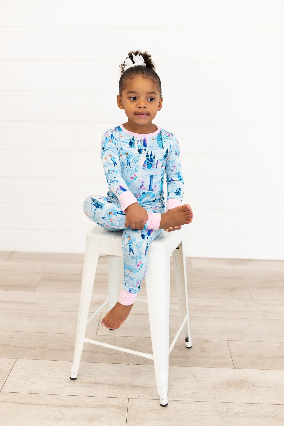 Two Piece Princess Pajama – The Wish Collection – on-model, girl sitting cross-legged on stool in blue castle-print pajamas