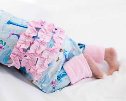 Baby Princess Pajama – The Wish Collection – on-model close-up of baby in blue castle-print zip pajama with pink ruffle