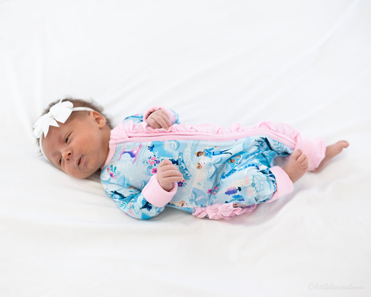 Baby Princess Pajama – The Wish Collection – on-model, sleeping newborn in blue castle-print zip pajama with pink ruffle