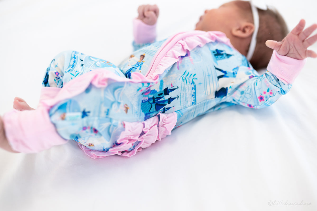 Baby Princess Pajama – The Wish Collection – on-model, newborn lying on back in blue castle-print zip pajama
