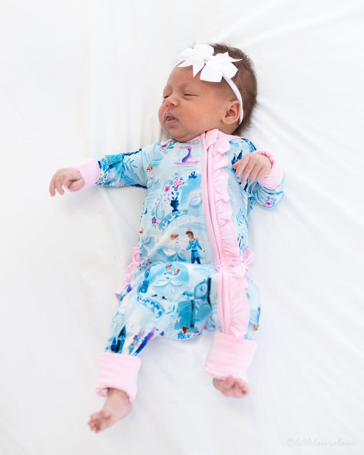 Baby Princess Pajama – The Wish Collection – on-model, sleeping newborn in blue castle-print zip pajama on white blanket
