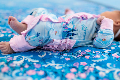 Baby Princess Pajama – The Wish Collection – close-up on-model of baby in blue castle-print zip pajama on floral blanket