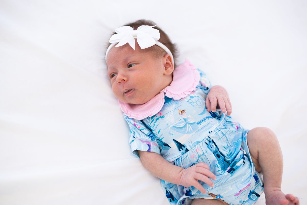 Baby Princess Dress – The Wish Collection – on-model, awake newborn in blue castle-print dress with pink ruffled collar